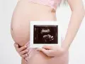 Ciężarna kobieta trzyma zdjęcie USG. To badanie, które pokazuje, co oznacza rozwój dziecka.
