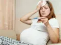 Ciężarna kobieta z termometrem i okładem na czole.