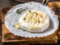 Topiony camembert w ciąży, zapiekany palnikiem z ziołami, na desce.