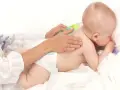 Dziecko w pieluszce leży na brzuchu, a dorosły delikatnie masuje mu plecy.