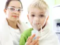 Dziecko z maską inhalatora, obok dziewczynka w okularach.