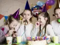 Radosne zabawy na urodziny! Dziewczynki w stożkowych czapkach dmuchają w gwizdki, śmiejąc się przy torcie z napisem "Happy Birthday".
