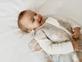 Uśmiechnięte dziecko w śpiworku z motywem króliczków i kwiatów. Widać jego rączki i twarz, a wszystko to na białym tle. To uroczy odruch galanta.