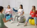 Ciężarne kobiety siedzą na piłkach gimnastycznych podczas zajęć w szkole rodzenia.