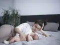 Matka karmi piersią dziecko na leżąco, opierając głowę na dłoni. Czuły moment bliskości.