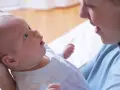 Uśmiechnięta mama patrzy na swoje 6 tygodniowe dziecko, które z zaciekawieniem spogląda w górę.