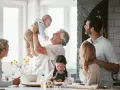 Rodzina w kuchni. Dziadek podrzuca wnuka, babcia patrzy z uśmiechem. Dzieci pomagają w przygotowaniach. To są babciowe dla kogo? Dla wszystkich, którzy kochają wspólne chwile.