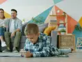 Chłopiec gra na telefonie, podczas gdy rodzice siedzą na kanapie. Ciekawe, od ilu lat jest WhatsApp i czy oni też go używają?