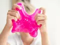 Dziecko bawi się różowym slime, rozciągając go. To świetna zabawa i prosty sposób, jak zrobić slime w domu.