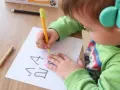 Dziecko w słuchawkach próbuje pisać na kartce.