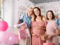 Trzy uśmiechnięte kobiety świętują baby shower. Jedna z nich jest w ciąży, a pozostałe dwie trzymają prezenty i balony.