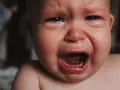 Malutkie dziecko płacze, ma zaczerwienione oczy i mokry nosek. To pewnie katar przy ząbkowaniu, który sprawia mu ból.