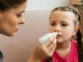 Mama delikatnie przykłada chusteczkę do nosa dziecka, na którym widać ślady krwi.
