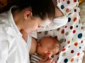 Matka karmi piersią noworodka, który właśnie skończył posiłek. To naturalny rytm, co ile karmić noworodka.