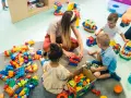 Dzieci bawią się klockami z opiekunką, co może być możliwe dzięki dofinansowaniu do żłobka. Radość i nauka przez zabawę.