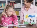 Dziewczynka z kredką w dłoni, smutna, podczas sesji socjoterapii. Terapeuta pokazuje jej rysunek.