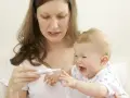 Zmartwiona mama mierzy temperaturę płaczącemu dziecku, które ma gorączkę po szczepieniu.