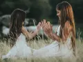 Dwie dziewczynki w białych sukienkach siedzą na łące i bawią się w "pajacyka". To idealna wyliczanka dla dzieci, która rozwija koordynację ruchową.