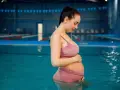 Kobieta w ciąży relaksuje się w basenie. Delikatne fale wody i spokój podkreślają jej błogostan. To idealny moment na odpoczynek, jak w domowym jacuzzi.