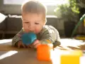 Zainteresowany 7 miesięczne dziecko bawi się kolorowymi klockami na dywanie w słoneczny dzień.
