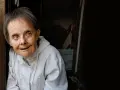 Portret kobiety z zespołem Downa w jasnej kurtce, patrzącej w bok.
