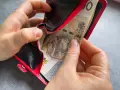 Ręce wkładają banknoty do czerwonego portfela. To może być 1000 zł na drugie dziecko, wsparcie dla rodziny.