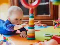 Zaintrygowany 6 miesięczne dziecko próbuje sięgnąć kolorowych kółek wieży.