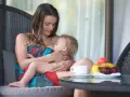 Matka karmi piersią dziecko na tarasie. Obok filiżanka kawy i owoce.