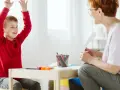Chłopiec z podniesionymi rękami, uśmiechnięty, podczas sesji terapeutycznej. Może to być pomocne w ocenie objawów ADHD u dzieci test.