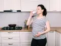 Ciężarna kobieta pije kefir w kuchni. To zdrowy napój dla przyszłych mam.