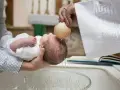 Chrzestna polewa główkę dziecka wodą święconą z muszli podczas ceremonii chrztu.