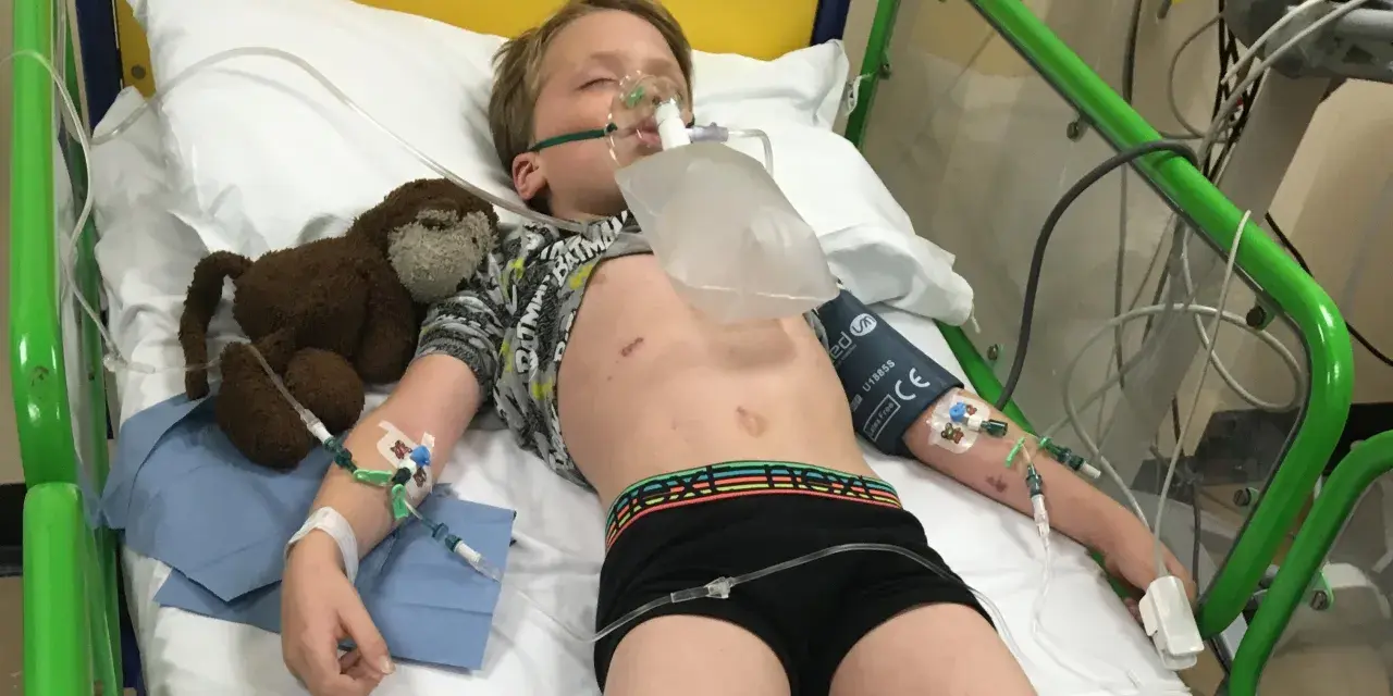 Chłopiec w szpitalnym łóżku z maską tlenową, podłączony do aparatury. To obraz walki z zapaleniem opon mózgowych u dzieci.