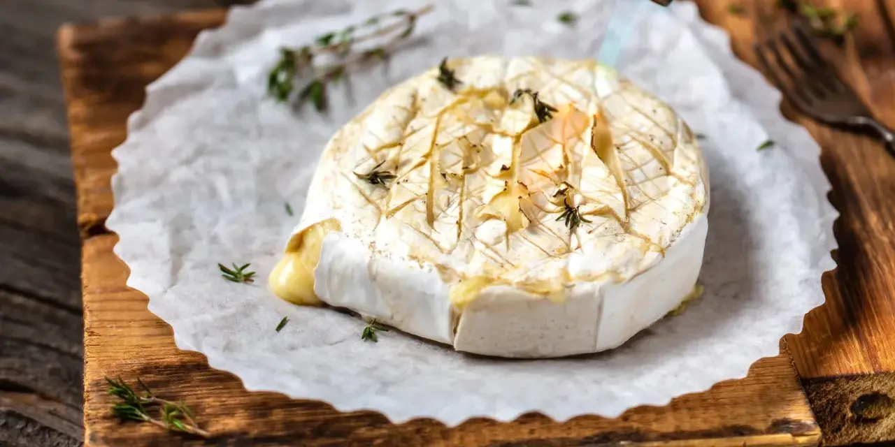 Topiony camembert w ciąży, zapiekany palnikiem z ziołami, na desce.