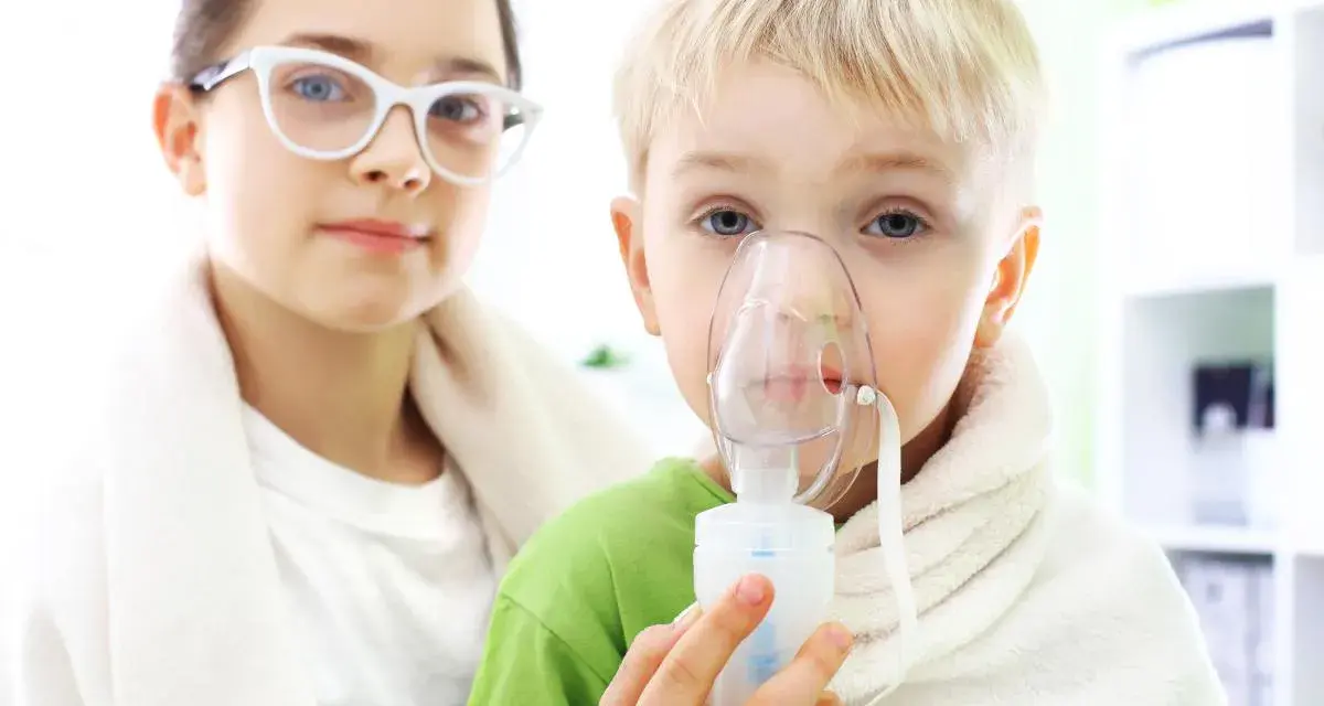 Dziecko z maską inhalatora, obok dziewczynka w okularach.
