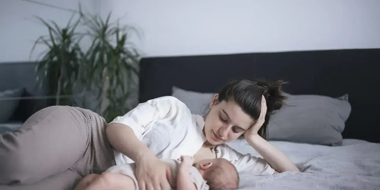 Matka karmi piersią dziecko na leżąco, opierając głowę na dłoni. Czuły moment bliskości.