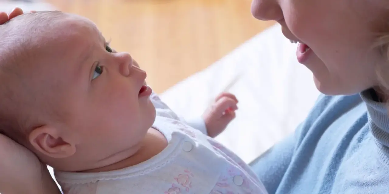 Uśmiechnięta mama patrzy na swoje 6 tygodniowe dziecko, które z zaciekawieniem spogląda w górę.
