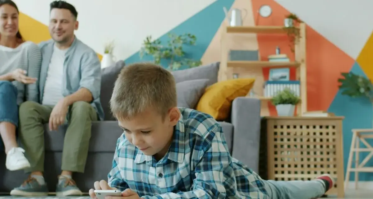 Chłopiec gra na telefonie, podczas gdy rodzice siedzą na kanapie. Ciekawe, od ilu lat jest WhatsApp i czy oni też go używają?