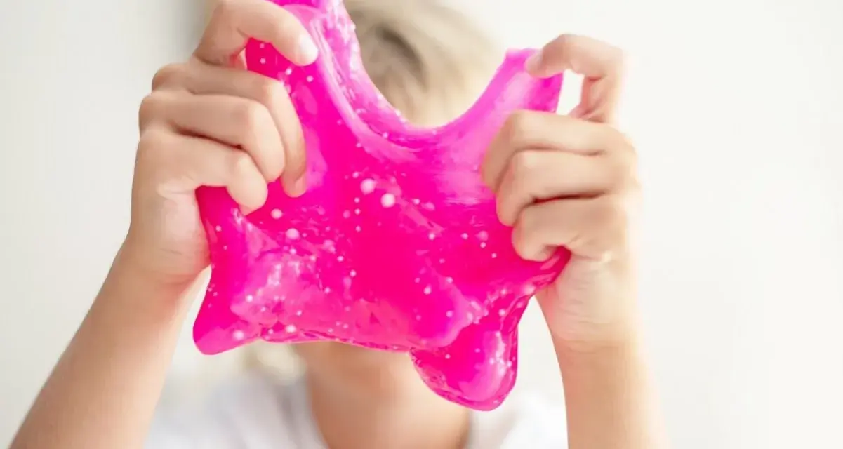 Dziecko bawi się różowym slime, rozciągając go. To świetna zabawa i prosty sposób, jak zrobić slime w domu.