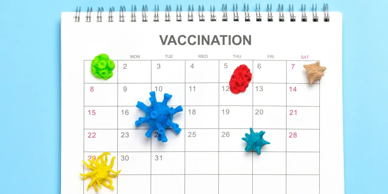 Kalendarz z napisem "VACCINATION" i kolorowymi modelami wirusów na dniach. Planowanie szczepień to klucz do pokonania pandemii.