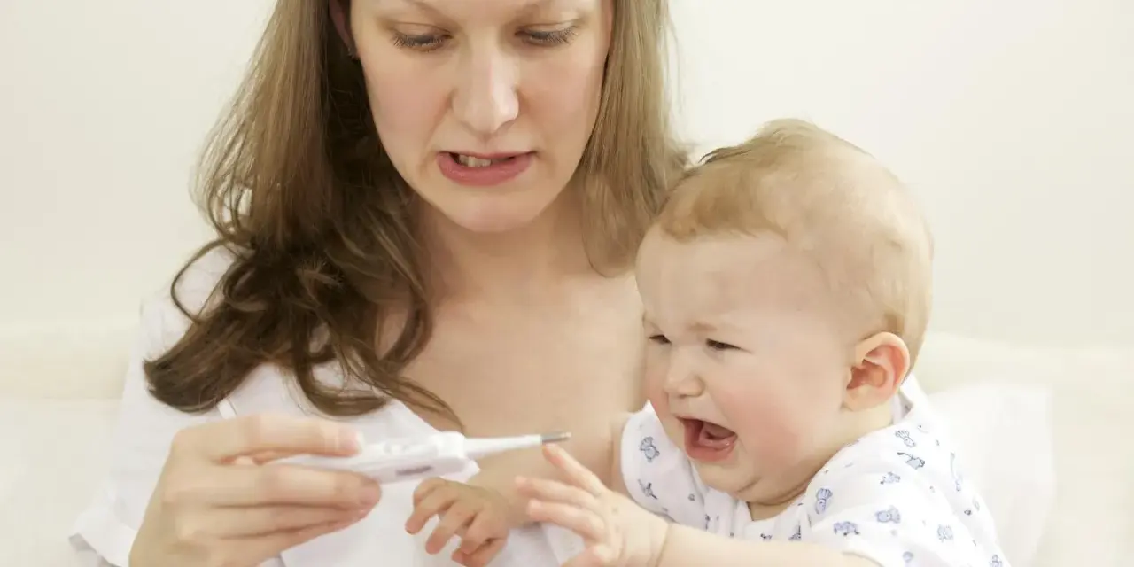 Zmartwiona mama mierzy temperaturę płaczącemu dziecku, które ma gorączkę po szczepieniu.
