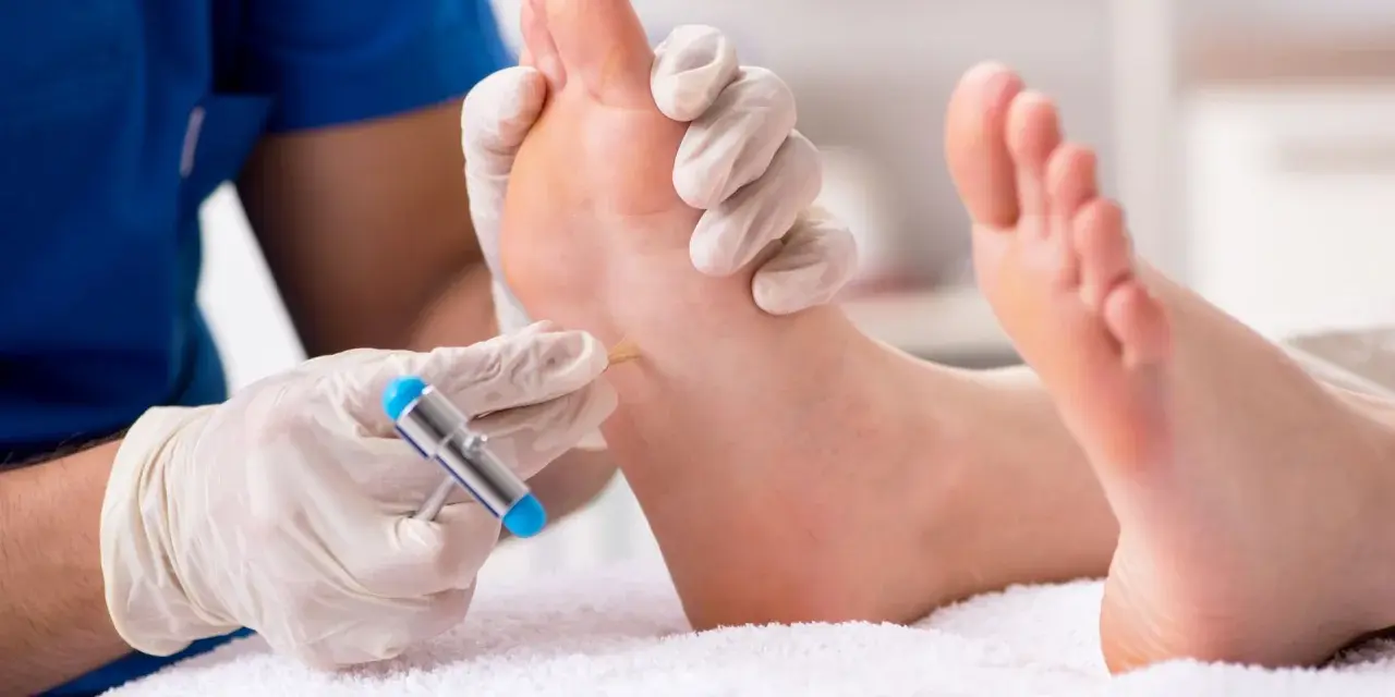 Lekarz w rękawiczkach bada stopę pacjenta młoteczkiem neurologicznym.