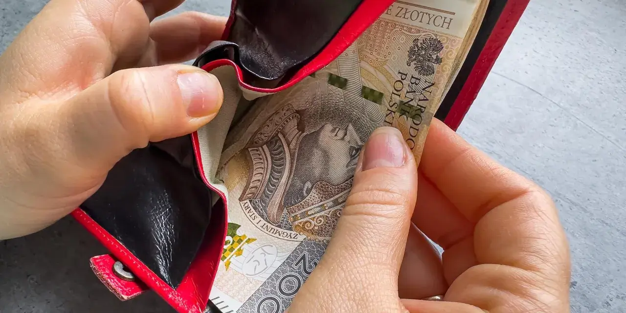 Ręce wkładają banknoty do czerwonego portfela. To może być 1000 zł na drugie dziecko, wsparcie dla rodziny.