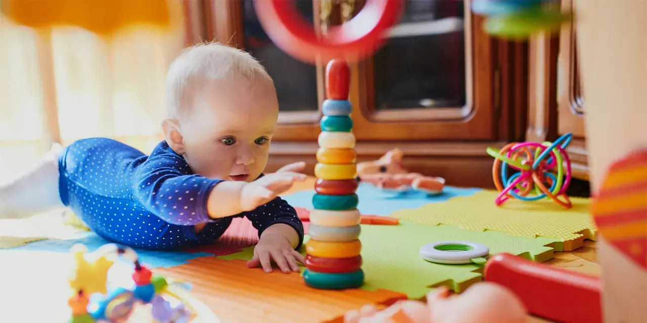 Zaintrygowany 6 miesięczne dziecko próbuje sięgnąć kolorowych kółek wieży.