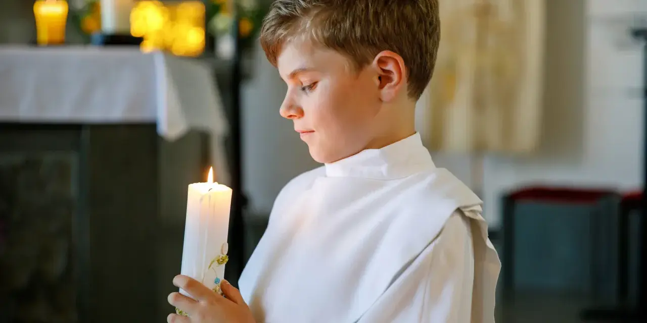 Chłopiec w białej szacie trzyma zapaloną świecę. To ważny moment, jak zorganizować chrzciny, by był niezapomniany.