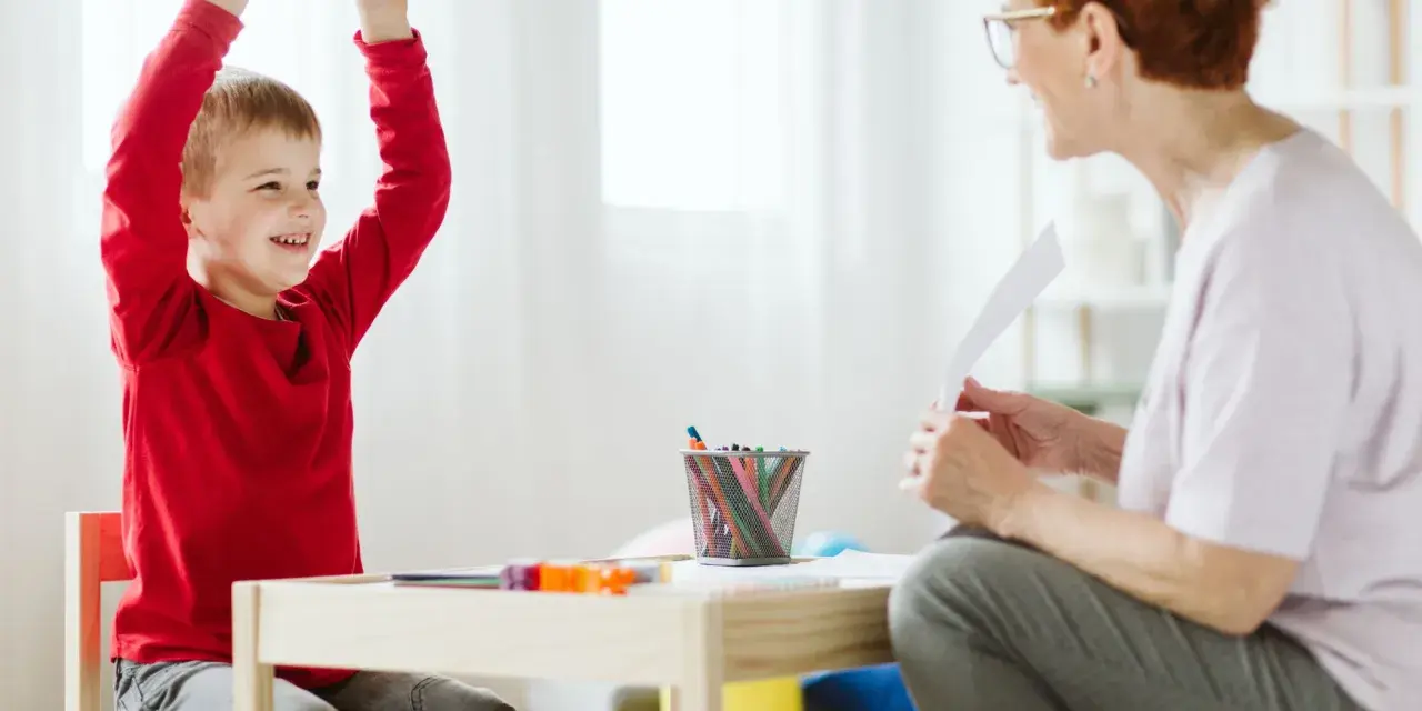 Chłopiec z podniesionymi rękami, uśmiechnięty, podczas sesji terapeutycznej. Może to być pomocne w ocenie objawów ADHD u dzieci test.