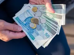 Ręce trzymają polskie banknoty 50 i 100 zł oraz monety. To może być kwota na bon oświatowy.
