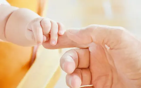 Dłoń dziecka chwyta palec dorosłego. Symbol nadziei i walki z zamartwicą urodzeniową.