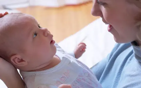 Uśmiechnięta mama patrzy na swoje 6 tygodniowe dziecko, które z zaciekawieniem spogląda w górę.