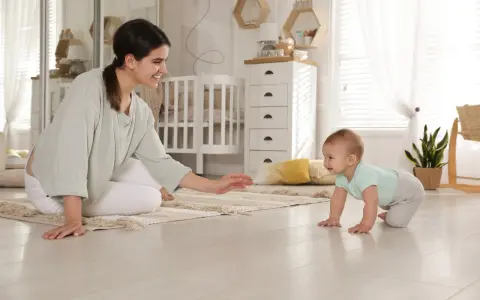 Uśmiechnięta mama zachęca do pierwszych kroków, kiedy dziecko raczkuje po dywanie w pokoju dziecięcym.