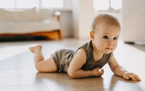 Dziecko w body leży na brzuchu na drewnianej podłodze, patrząc w bok.